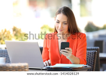 Entrepreneur checking smart phone working with a laptop in a coffee shop
