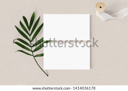 Blank white business cards mockups with palm leaf and silk ribbon on textured table backgound. Elegant modern template for branding identity. Tropical design. Wedding stationery. Flat lay, top view. Royalty-Free Stock Photo #1414036178