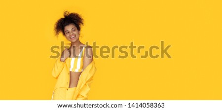 Playful happy young african woman wear stylish yellow clothes look aside at copy space, black teen girl curious about fashion sale on summer studio background, horizontal banner header website design