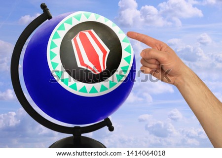 Male hand in the pointing gesture facing the globe which shows the blue flag of the state of bougainville on a background of bright sky with clouds