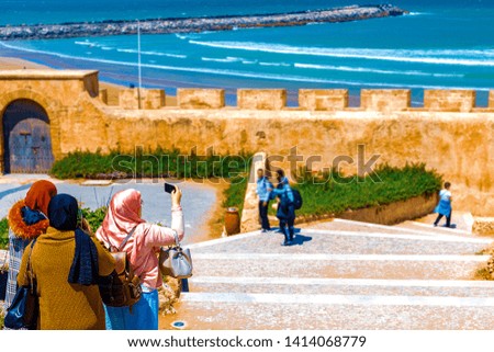 Three Arab girls spend time together in the fresh air, walking in the afternoon along the embankment of the city and taking pictures of the ocean on a smithphone. Rabat, Morocco, Africa