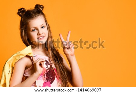 portrait of a cute, charming, attractive, cheerful teenage girl, showing a V-sign on a yellow background and holding a jacket. Fashionable kids concept