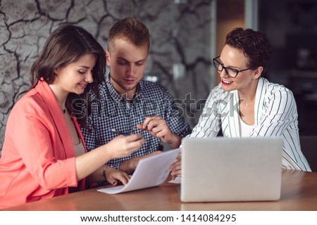 Investment adviser giving a presentation to a friendly smiling young couple seated at her desk in the office
