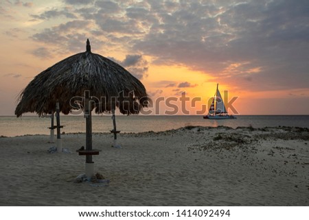 Grass Umbrellas at Beautiful Palm Beach and a Sailing Boat on Sea in Aruba Island Netherland Antilles During Sunset