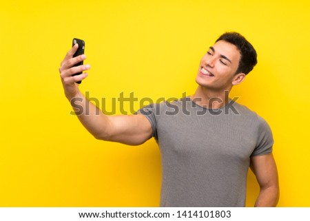 Handsome man over isolated yellow wall making a selfie