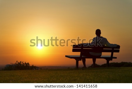 Portrait of a man sitting on a bench enjoying the Sunset Royalty-Free Stock Photo #141411658