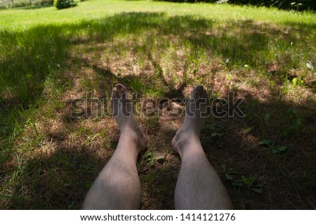 Picture of the feet and legs of someone sitting in the shade of a big tree in a park on a very sunny and warm day.  Good place to rest and relax.