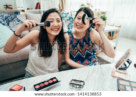 Female friends putting makeup while preparing for vacation trip with suitcase. young girls face camera having fun with cosmetic product brush posing smiling laughing joyful. women get ready at home