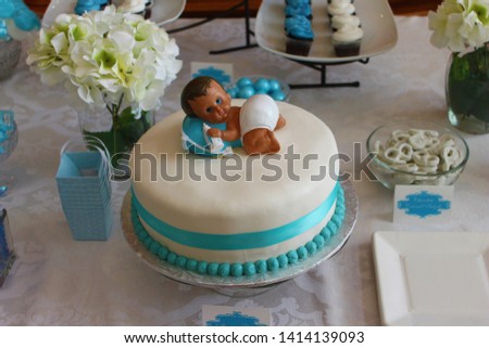 Picture of a baby on a blue and white cake. With cupcakes in the background with flowers on a table.