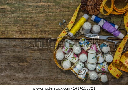 Spools of thread and basic sewing tools including pins, needle, a thimble, and tape measure on an old wooden tabletop. concept with copy space.