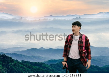Young hipster photographer holding a camera with beautiful foggy winter sunrise in mountains natural background.