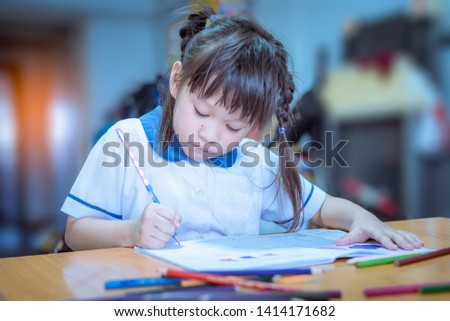 A happy asian girl is painting homework picture with verity crayon color on the table.