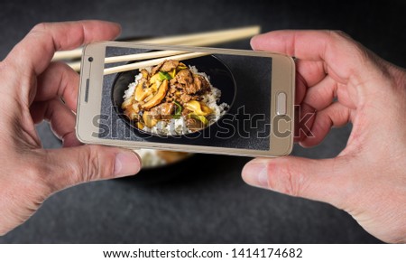 Man taking photo of Chinese rice with beef meat and vegetagles on dark background