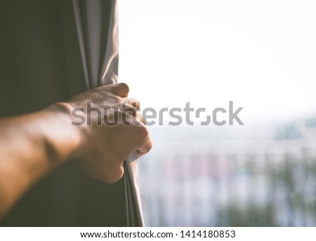 The young man opens the white curtain and Looking through the window glass outside in the morning, Curtain interior decoration in the living room, hope concept.