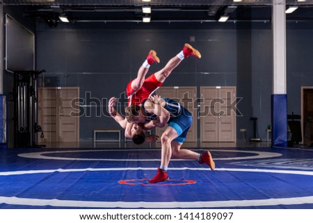 Two young men in blue and red wrestling tights are wrestlng and making a hip throw on a yellow wrestling carpet in the gym. The concept of fair wrestling