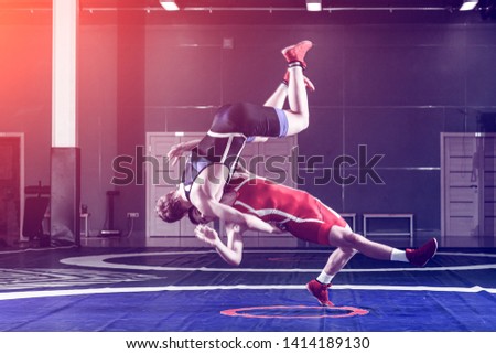 Two young men in blue and red wrestling tights are wrestlng and making a suplex wrestling on a yellow wrestling carpet in the gym. The concept of fair wrestling