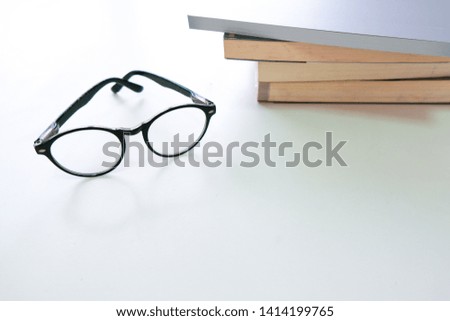 Black eye glasses are placed on a stack of books on a white wooden table beside the window.