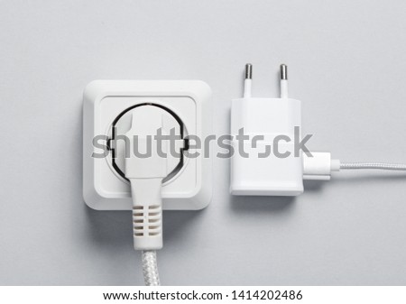 The concept of electrical dependence. The plug is plugged into the power outlet and the charger on a gray background. Top view