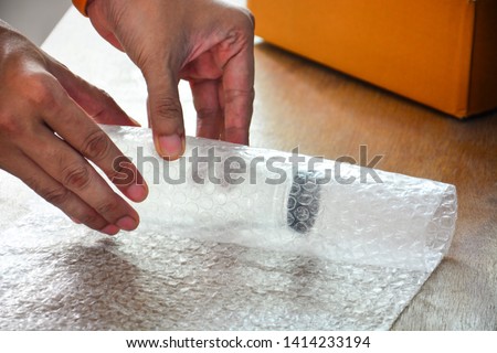 close up of a guy's hands using bubble wrap to pack a glass bottle before put into cardboard box deliver to customer, e commerce shipping, online business trading concept Royalty-Free Stock Photo #1414233194