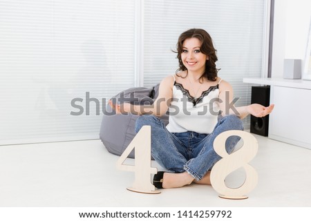 A young beautiful Caucasian woman sits on a floor in a modern living room with wooden signs in the form of numbers 48. Numerology, meaning of numbers, magic