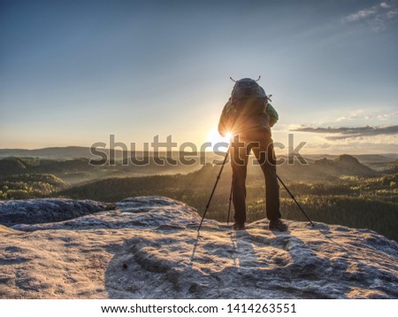 Artist set camera and tripod to photograph the sunrise on a rocky summit. Artist works in nature