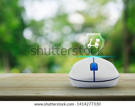 Motorcycle with shield flat icon on wireless computer mouse on wooden table over blur green tree in park, Business motorbike insurance online concept