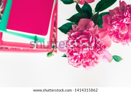 bouquet of pink peonies, a stack of books, pencils and a notebook on a white table, top view