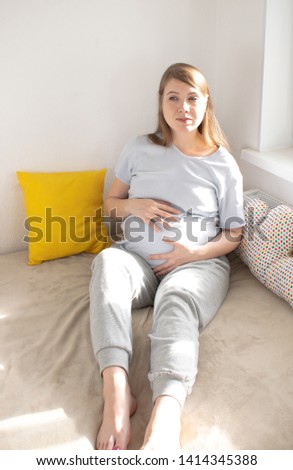 Happy young pregnant woman sitting in bed touches hands to her belly. The concept of childbirth, prenatal medicine, motherhood.