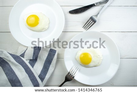 traditional breakfast of two fried eggs. White plate with eggs on the background of a white wooden table. Concept image of breakfast, healthy eating.