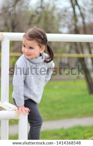 little cheerful brunette girl in a sweater and with tails is standing on a metal structure on construction site