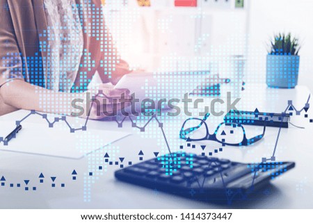 Hands of woman working with tablet at office table with double exposure of world map and graphs. Concept of trading and stock market. Toned image