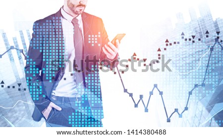 Bearded man in suit looking at smartphone over cityscape background with double exposure of world map and graphs. Stock market and trading concept. Toned image