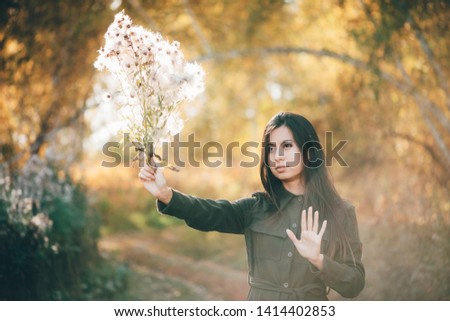 Dreamy beautiful girl with thistle flowers bouquet in golden sunlight on bokeh background with yellow leaves. Inspired girl enjoys sunset in autumn forest. Female beauty portrait among autumn foliage.