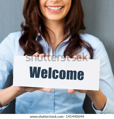 Smiling woman showing white card with welcome word in a close up shot