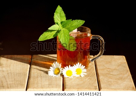 Tea with fresh mint leaves in a glass, shot close-up on a wooden table and a black background behind it