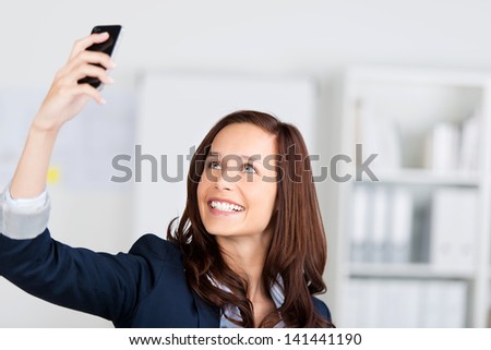 Woman photographing herself with her mobile phone holding it up in the air and smiling