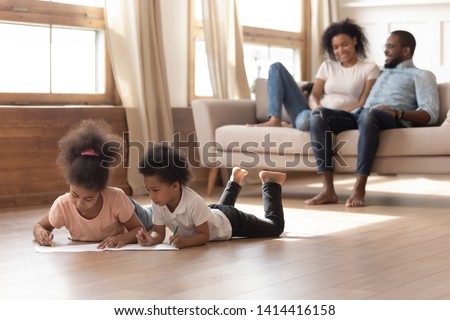 Happy african american family with kids leisure lifestyle activities in modern living room concept, young black parents relax talk sit on sofa children drawing playing on warm wooden floor at home