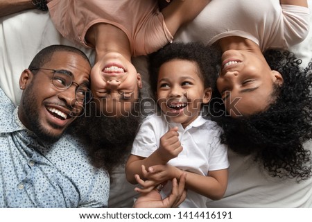 Affectionate african american parents and cute small kids laughing lying on bed together, happy mixed race family with children bonding having fun enjoy funny moments in bedroom, top view from above