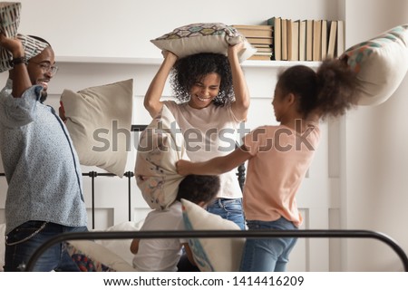 Happy playful african american family and little cute kids having fun pillow fight on bed, black parents with small funny mixed race preschool children laugh play leisure game in bedroom on weekend