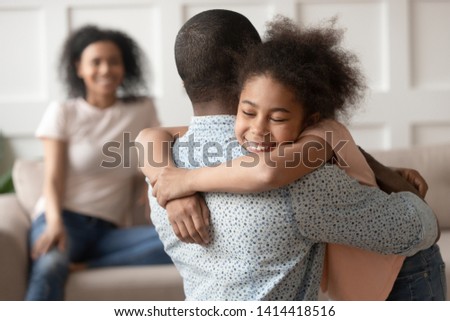 Happy cute little african american kid daughter embracing black dad at home, funny small mixed race child and father hugging cuddling, daddy and child love connection, family reunion, joint custody Royalty-Free Stock Photo #1414418516