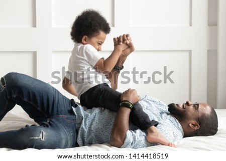 Happy african american family single dad laugh play with little son on bed, cute small kid boy having fun with black father tickle cuddle bonding in bedroom, child and daddy funny leisure moments