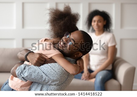 Happy african american dad embracing daughter cuddling at home, smiling black father hugging cute little kid girl bonding enjoy time together, daddy child reunion, fatherhood, child custody concept Royalty-Free Stock Photo #1414418522