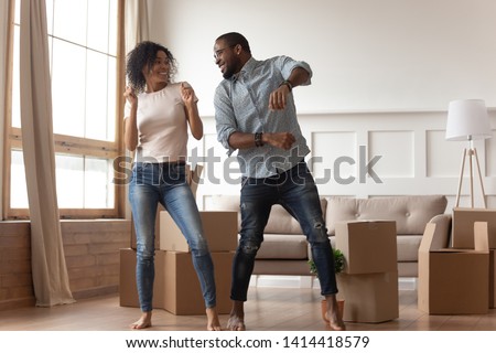 Happy carefree african couple first time home buyers renters owners dancing laughing in living room with boxes together, funny black tenants having fun enjoy relocation in new house on moving day Royalty-Free Stock Photo #1414418579