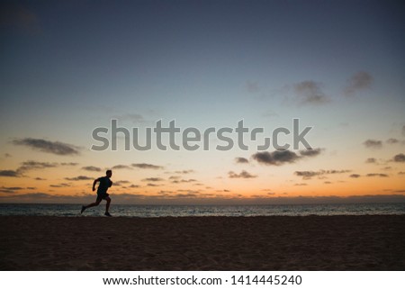 A side-view shot of a caucasian mid-adult man jogging across the beach in Perth, Australia. The sun is setting behind him.