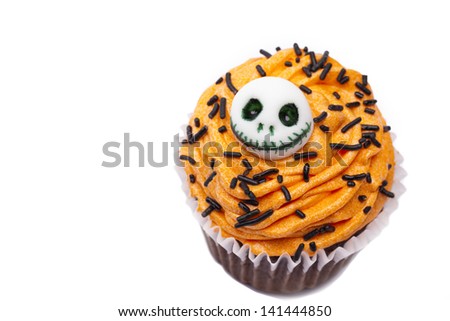 Close-up top view of a orange cupcake with skull design and brown icing over white background.