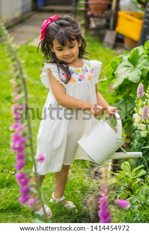 Four year old girl model gardening and playing in an English garden in early summer during the daytime. 