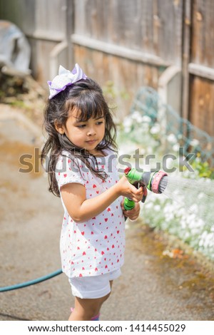 Four year old girl model gardening and playing in an English garden in early summer during the daytime. 