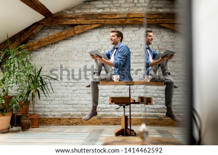 Handsome young man using digital tablet while sitting on the table in the rustic room