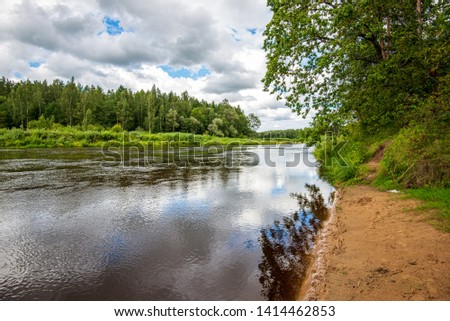 calm countryside lake river with cloud reflections in water and green shores with trees and foliage