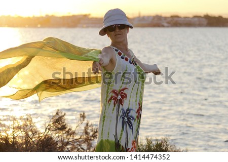 Mature woman, with hat playing with a handkerchief by the sea  in the wind by the sea at sunset, next to the salt flats  in the Mar Menor, Murcia, Spain, holidays, milf, holidays,